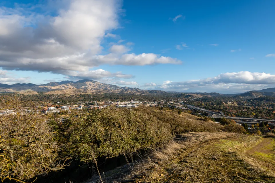 A broad valley with two tall peaks in the background. In the foregound, but far below the view from the hill where the photo was taken, large freeways are visible.